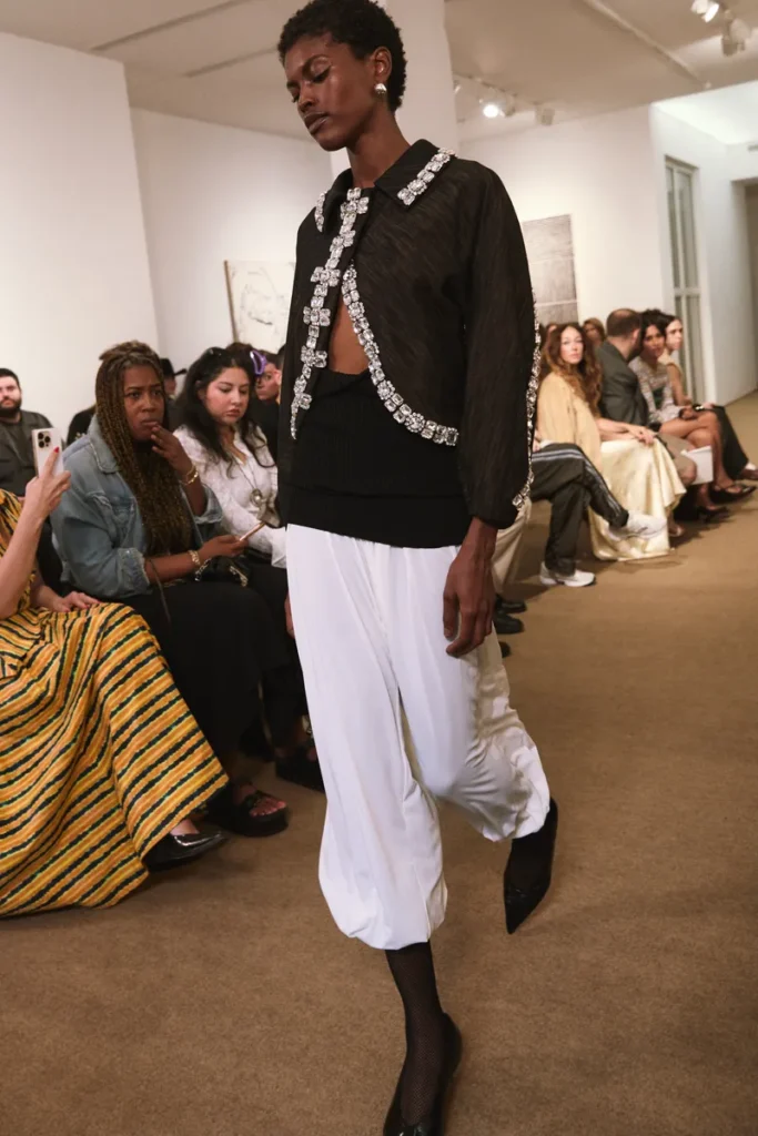 مدل با ژاکت مشکی کریستال‌دوز و شلوار سفید از Amir Taghi Spring 2026 در New York Fashion Week